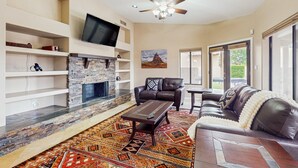 A living room with a stone fireplace, leather sofa, and a television mounted on the wall. - Peoria Paradise: Poolside Vibes & Family Good Times. Spacious Backyard with Pool (Peoria)