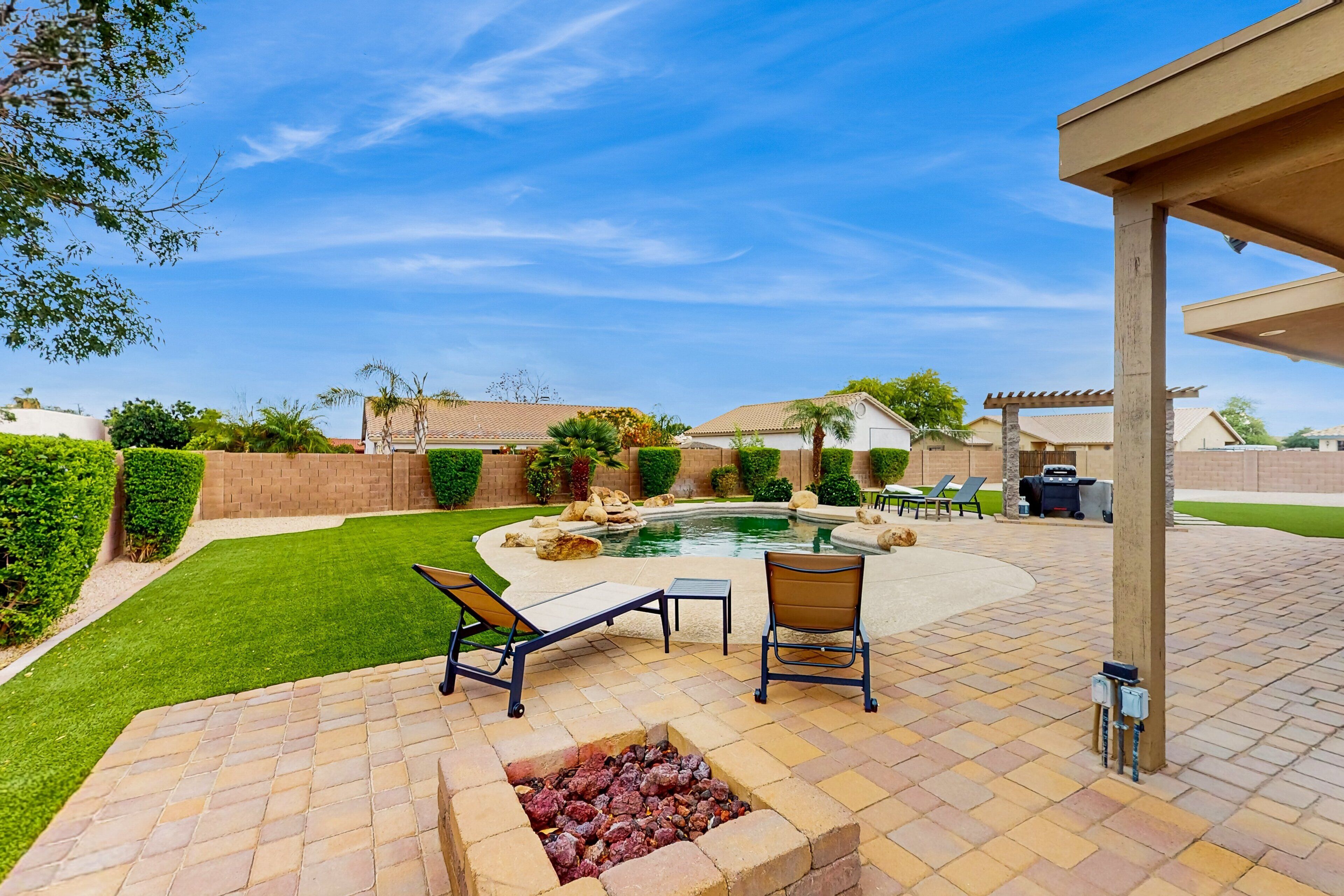 A backyard with a swimming pool, lounge chairs, a fire pit, and a pergola.