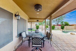 Un patio techado con una mesa y sillas, una lámpara de techo y vistas a una piscina y jardín.