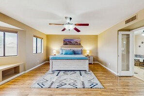 Un dormitorio con cama, ventilador de techo, mesita de noche, ventana y puerta.