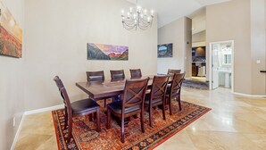 A dining area with a large wooden table, six chairs, and a chandelier. There are two paintings on the wall and a rug on the floor. - Peoria Paradise: Poolside Vibes & Family Good Times. Spacious Backyard with Pool (Peoria)