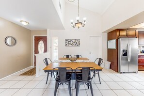Un comedor con una mesa de madera, sillas negras, una araña y un refrigerador de acero inoxidable.