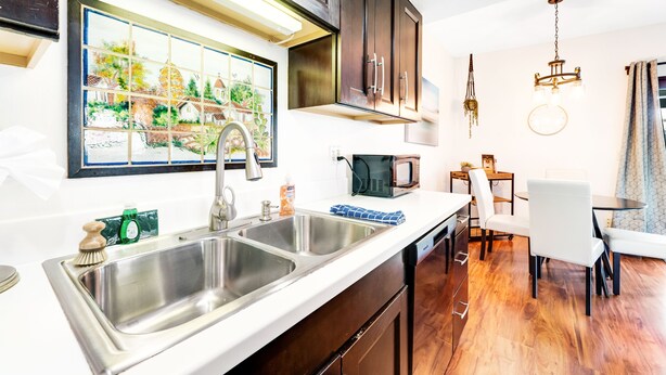 A modern kitchen with stainless steel sinks, a microwave, and a dining area with a table and chairs. - Dog-friendly townhouse with enclosed patio, outdoor pool, mtn views, W/D, AC (Phoenix)