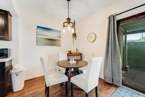 Een eetruimte met een ronde tafel, witte stoelen, een kroonluchter, een klok en uitzicht door een glazen deur.