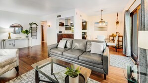 A modern living room with a grey sofa, a glass coffee table, and a dining area with a table and chairs. - Dog-friendly townhouse with enclosed patio, outdoor pool, mtn views, W/D, AC (Phoenix)