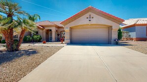 A single-story house with a red-tiled roof, a garage, and a driveway leading to the entrance. - Inviting home with full kitchen, patio, central AC, & W/D (Sun City West)