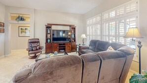A living room with a brown leather sofa, a brown leather armchair, a wooden entertainment center with a flat-screen TV, and a floor lamp. - Inviting home with full kitchen, patio, central AC, & W/D (Sun City West)