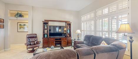 A living room with a brown leather sofa, a brown leather armchair, a wooden entertainment center with a flat-screen TV, and a floor lamp.
