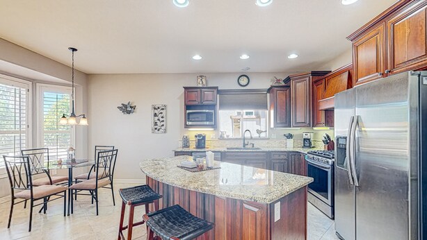 A kitchen with wooden cabinets, a stainless steel refrigerator, a microwave, and a large island with bar stools. - Inviting home with full kitchen, patio, central AC, & W/D (Sun City West)