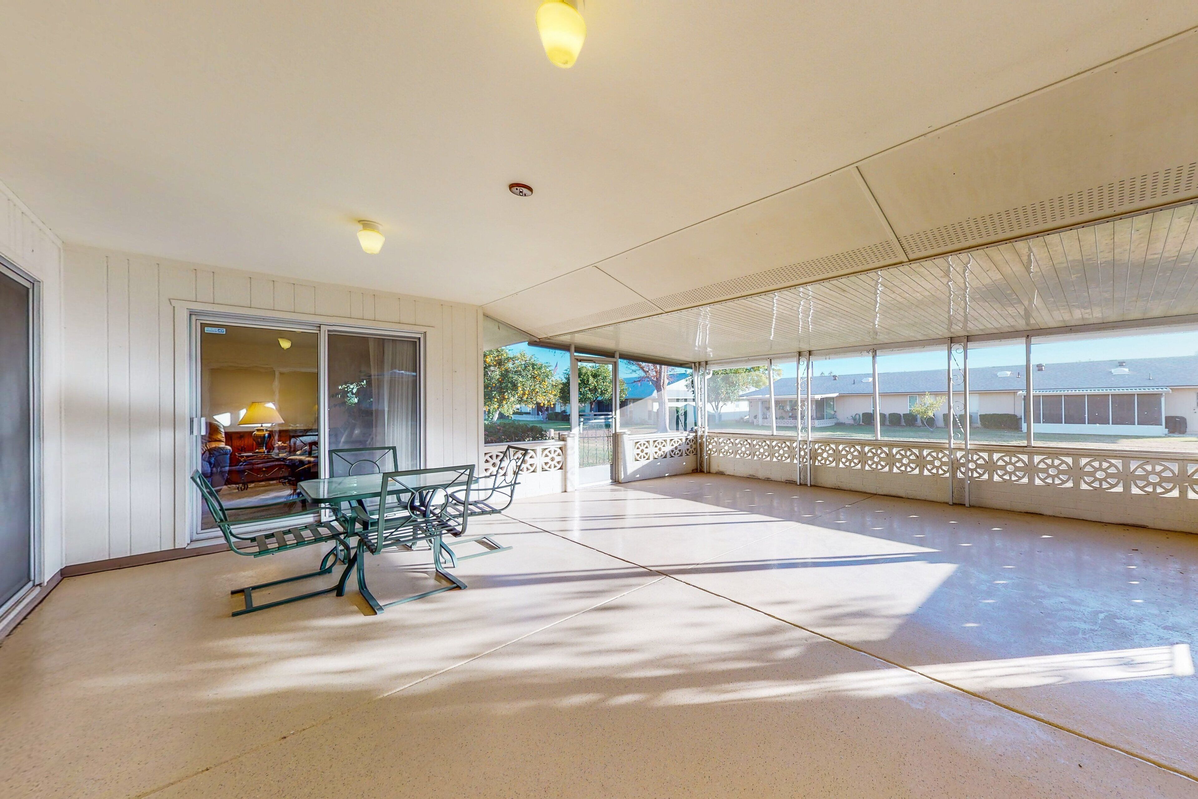 A spacious covered patio with a table and chairs, large windows, and a view of the surrounding area.