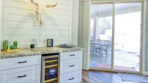 A kitchen with a white cabinet, a glass-fronted dishwasher, a bull skull mounted on the wall, and a sliding glass door leading to an outdoor patio. - Private desert dream home with enclosed yard, pool, furnished lanai, & grill (Mesa)