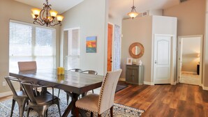 A dining area with a wooden table, chairs, and a chandelier. There are windows with blinds, a rug, and a door leading to another room. - Private desert dream home with enclosed yard, pool, furnished lanai, & grill (Mesa)
