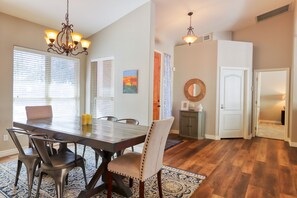 A dining area with a wooden table, chairs, and a chandelier. There are windows with blinds, a rug, and a door leading to another room. - Private desert dream home with enclosed yard, pool, furnished lanai, & grill (Mesa)