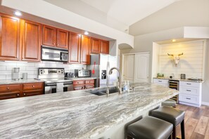 A kitchen with wooden cabinets, stainless steel appliances, a marble countertop, and a bull skull decoration. - Private desert dream home with enclosed yard, pool, furnished lanai, & grill (Mesa)