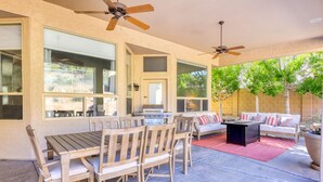 An outdoor patio with a wooden table and chairs, a black coffee table, a white sofa with red and white cushions, and a large potted plant. - Private desert dream home with enclosed yard, pool, furnished lanai, & grill (Mesa)