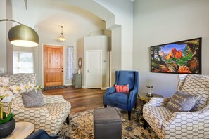A living room with patterned sofas, a blue armchair, and a large painting on the wall. - Private desert dream home with enclosed yard, pool, furnished lanai, & grill (Mesa)