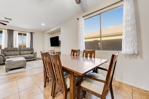 A dining area with a wooden table and chairs, a sofa, and a TV mounted on the wall. - Mountain-view gem - 2 large living rooms, heated pool, enclosed yard, AC & W/D (Avondale)