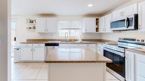 Una cocina moderna con armarios blancos, encimera de granito, horno empotrado, microondas y lavavajillas.