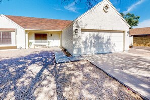 A single-story house with a garage, a front porch, and a gravel driveway. - Charming home near walking paths with a work desk, grill, & patio - dog-friendly (Tempe)