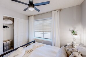 A bedroom with a bed, a ceiling fan, a window with blinds, a nightstand with a lamp, and a wardrobe. - Charming home near walking paths with a work desk, grill, & patio - dog-friendly (Tempe)