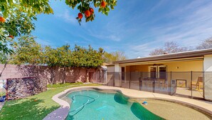 A swimming pool with a stone wall and a glass fence, surrounded by a well-maintained lawn and trees. - Modern home with open layout, private pool, & washer/dryer - dog friendly (Phoenix)