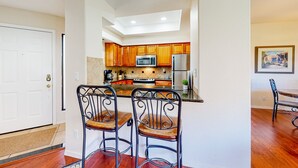 A kitchen with wooden cabinets, a microwave, a refrigerator, and two metal chairs with wooden seats. - Beautiful condo with stunning views, pool, hot tub, balcony, W/D, AC (Tucson)
