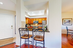 A kitchen with wooden cabinets, a microwave, a refrigerator, and two metal chairs with wooden seats. - Beautiful condo with stunning views, pool, hot tub, balcony, W/D, AC (Tucson)