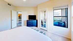 A bedroom with a bed, a dresser, a television, and a sliding glass door leading to an outdoor area. - Beautiful condo with stunning views, pool, hot tub, balcony, W/D, AC (Tucson)