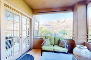 A balcony with a green sofa, a white vase, and a view of mountains.