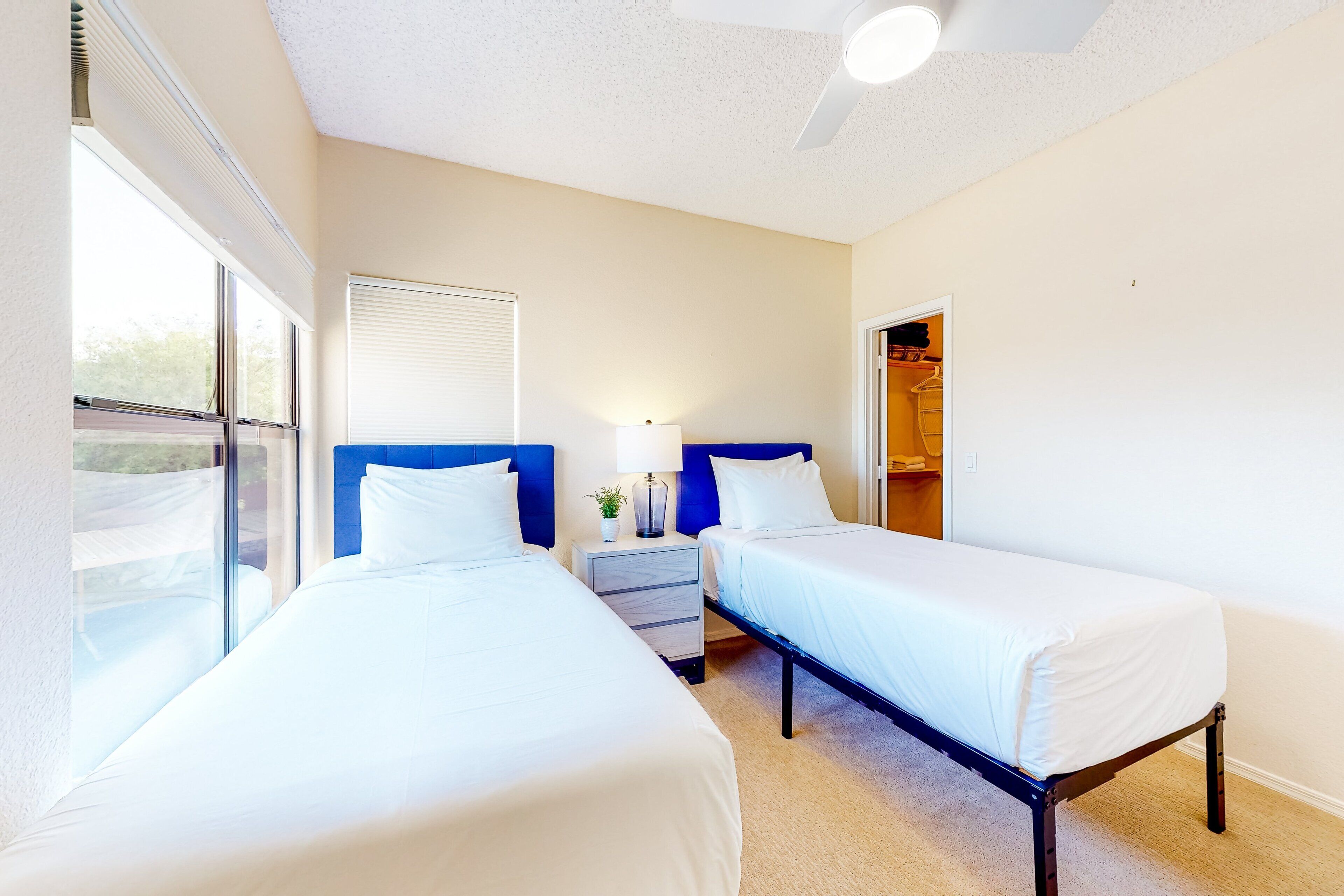 A bedroom with two beds, a nightstand with a lamp, and a closet.