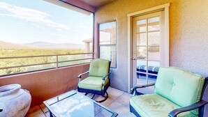A balcony with two green chairs, a glass table, and a view of a desert landscape. - Beautiful condo with stunning views, pool, hot tub, balcony, W/D, AC (Tucson)