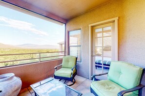 A balcony with two green chairs, a glass table, and a view of a desert landscape. - Beautiful condo with stunning views, pool, hot tub, balcony, W/D, AC (Tucson)