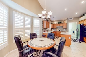 A modern kitchen with a central island, black leather chairs, and a chandelier. - Palm-lined home with pool access, grill, office & golf course views (Sun Lakes)