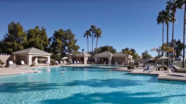 Una piscina con sillas de descanso y palmeras al fondo.