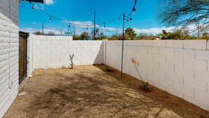 A fenced outdoor area with a gravel ground, a white brick wall, and a street sign indicating 'Cherry Ave 3200 N'. - Inviting dog-friendly studio with full kitchen and central AC (Tucson)