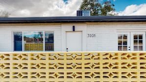 A building with a white brick facade, numbered 3201, featuring large windows and a yellow patterned fence. - Inviting dog-friendly studio with full kitchen and central AC (Tucson)