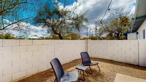 An outdoor patio area with two blue chairs and a table, surrounded by a white brick wall. - Inviting dog-friendly studio with full kitchen and central AC (Tucson)
