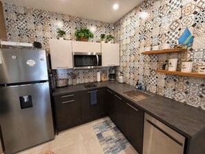 Une cuisine moderne dotée d’un réfrigérateur en acier inoxydable, d’un four à micro-ondes et de meubles de rangement aux couleurs sombres.