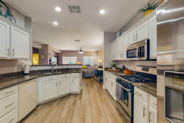 A modern kitchen with white cabinets, granite countertops, stainless steel appliances, and a wooden floor. - inviting home with private pool, patio, grill, washer/dryer, & central AC (Chandler)