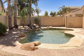Ein Pool mit gewölbter Kante, umgeben von Palmen und einem Pflasterweg.
