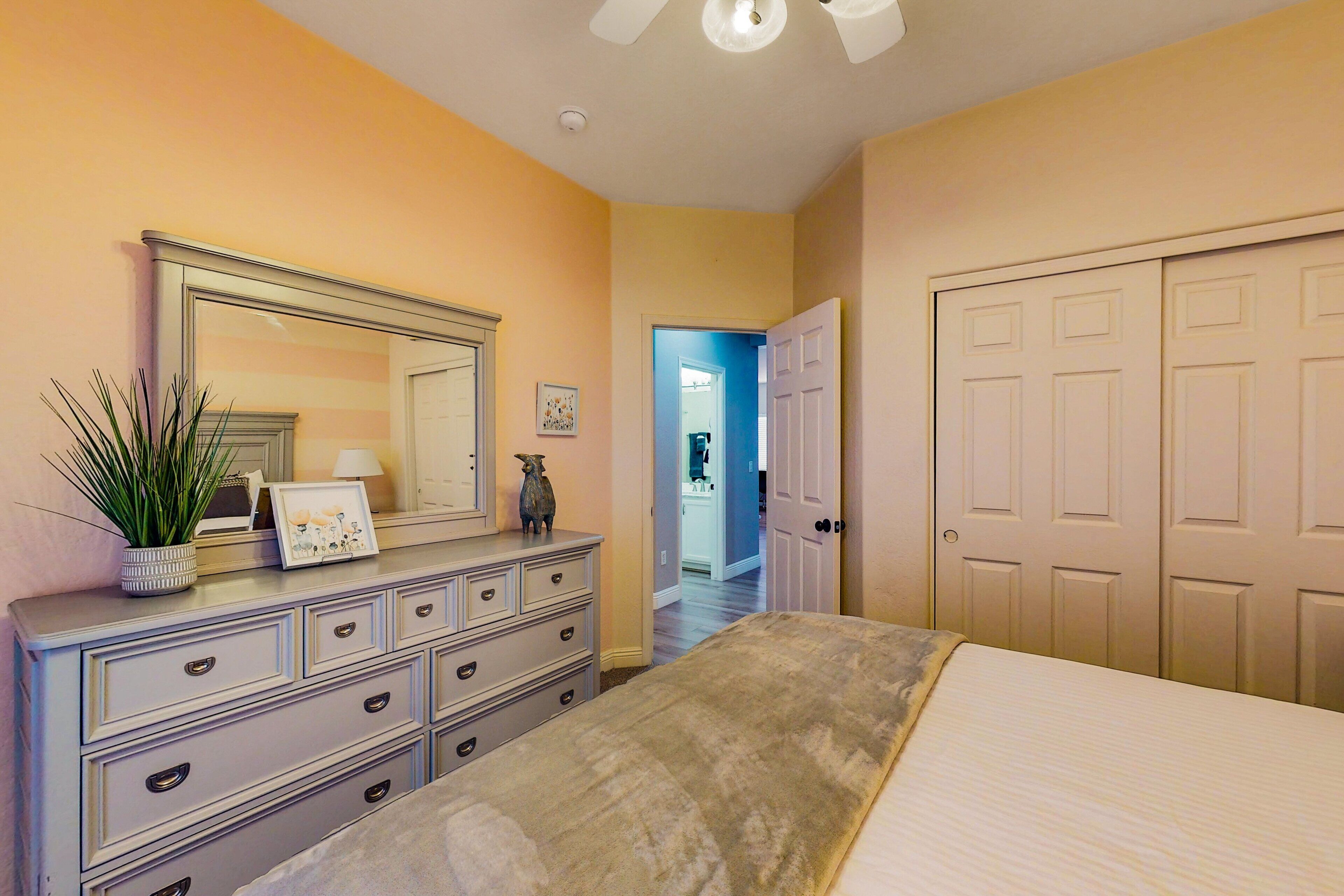 A bedroom with a bed, dresser, mirror, and a hallway leading to another room.