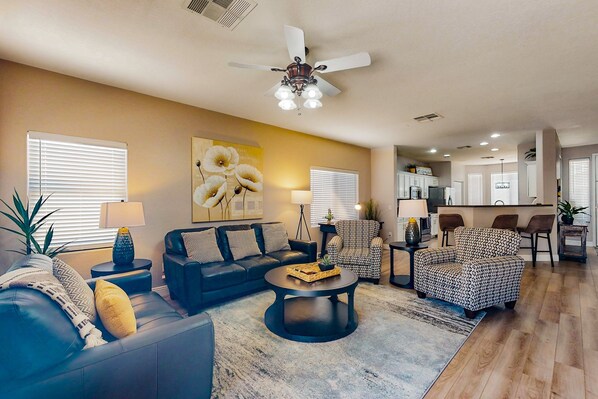 A living room with a sofa, armchairs, a coffee table, and a ceiling fan. There is a kitchen area in the background. - inviting home with private pool, patio, grill, washer/dryer, & central AC (Chandler)
