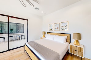 A modern hotel room with a large bed, a glass wall, and a balcony with stools.