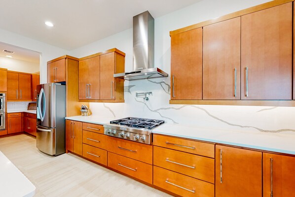 A modern kitchen with wooden cabinets, a stainless steel refrigerator, and a gas stove.