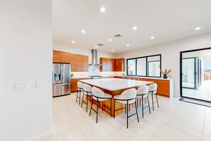 A modern kitchen with a central island, wooden cabinets, stainless steel appliances, and a large window.