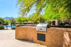 Un espace barbecue extérieur avec un mur en pierre, un gril et un parasol.
