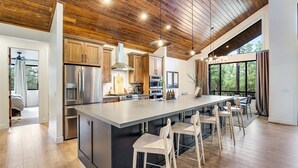 Een moderne keuken met houten plafond, roestvrijstalen apparatuur en een groot eiland met barkrukken.