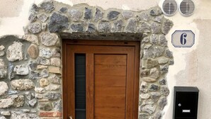 Une porte en bois, un mur en pierre, une petite boîte aux lettres et une grille d’aération sur le mur.