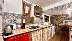 Une cuisine compacte avec un réfrigérateur rouge, une cuisinière à gaz et un évier. Il y a une petite fenêtre au-dessus de l’évier et un meuble en bois au-dessus de la cuisinière.