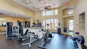 A spacious gym with various exercise machines, large windows, and an exit sign.